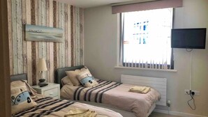 Une chambre avec deux lits, un téléviseur, une fenêtre avec des stores et un panneau mural en bois.