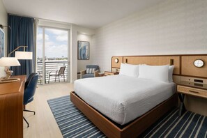 A hotel room with a large bed, a desk with a lamp, a chair, a nightstand, and a view of the outdoors. - Near Airport with Free Shuttle & Pool Vibes (Fort Lauderdale)