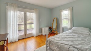 Une chambre à coucher comprenant un lit, une commode, une coiffeuse avec un miroir et une fenêtre avec des rideaux.