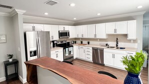 Una cocina moderna con armarios blancos, electrodomésticos de acero inoxidable y una isla de madera con un jarrón azul.