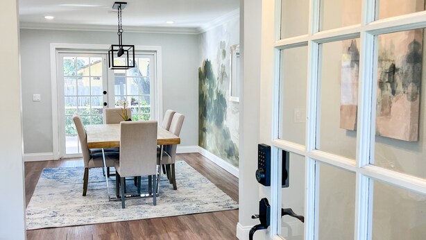 Un área de comedor con una mesa de madera, sillas y un tapete. Hay una puerta con paneles de vidrio satinado y cerradura con tarjeta.