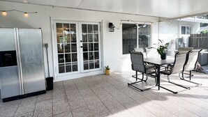 Un área de patio techada con una mesa y sillas, un refrigerador y una planta en maceta.