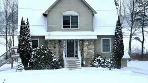 A two-story house with a stone foundation, a front porch, and a snow-covered roof. - Home in Mount Pocono, Hot tub, Sauna, Lakefront, Kayaks+ (Pocono Summit)
