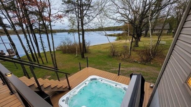 A hot tub on a wooden deck with a view of a lake and trees. - Home in Mount Pocono, Hot tub, Sauna, Lakefront, Kayaks+ (Pocono Summit)