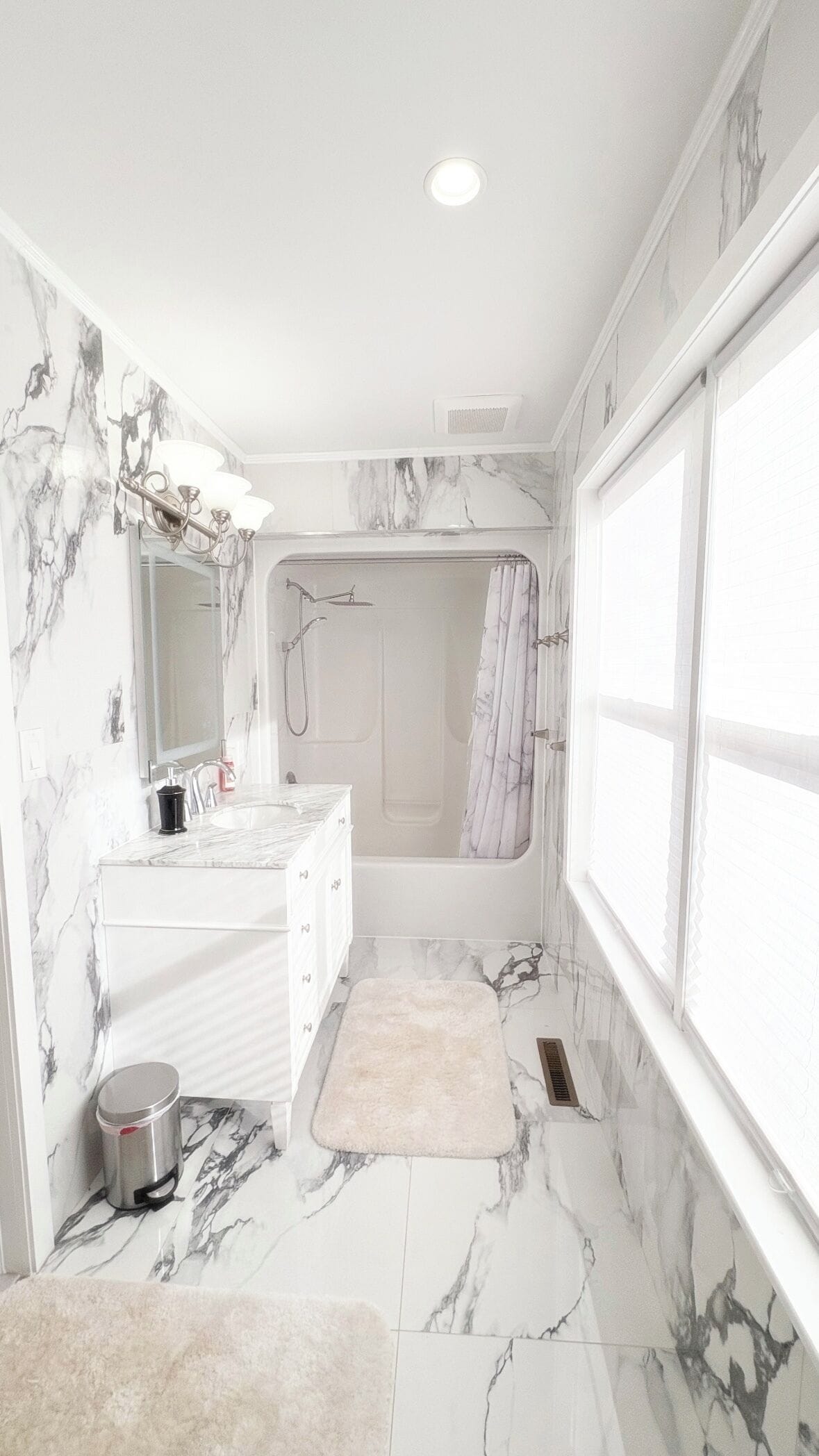 A bathroom with a marble floor, a shower, a sink with a mirror, and a window.