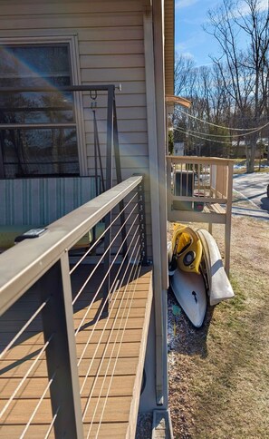 Eine Holzterrasse mit Metallgeländer, ein überdachter Veranda-Bereich und ein Kajak, das an das Haus gelehnt ist.