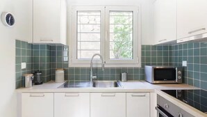 A modern kitchen with white cabinets, a stainless steel sink, a microwave, and a window with a view of greenery. - Apartment with Leafy Backyard Steps from the Acropolis (Athens)