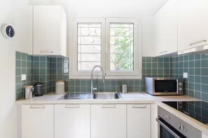 Eine moderne Küche mit weißen Schränken, einer Edelstahlspüle, einer Mikrowelle und einem Fenster mit Blick auf Grünflächen.