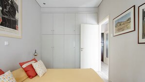 A bedroom with a bed, pillows, a wardrobe, and a door leading to another room. - Apartment with Leafy Backyard Steps from the Acropolis (Athens)