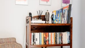 A cozy reading nook with a wooden bookshelf filled with books, a patterned throw pillow, and a small decorative item on the shelf. - Apartment with Leafy Backyard Steps from the Acropolis (Athens)