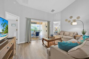 A spacious living room with a sofa, coffee table, and a TV. There is a sliding glass door leading to an outdoor area. - Davenport 4BR Villa, Pool, Game Room, Near Disney & Shopping (Davenport)