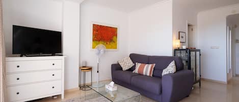 A living room with a flat-screen TV, a sofa, a coffee table, and a painting on the wall.