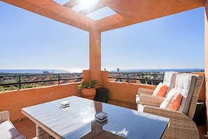 Ein Balkon mit Glastisch, Korbmöbeln und Blick auf die Stadtlandschaft.