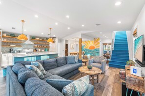 A modern living room with a large gray sectional sofa, a wooden coffee table, and a blue staircase. - Sugar Shack*Designer*PrivatePool*BeachService (DESTIN)