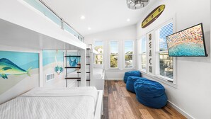 Un dormitorio moderno con literas, un ventanal con persianas, un ventilador de techo y un mural de temática playera.
