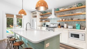 Una cocina moderna con una isla grande, armarios blancos y vistas a una piscina.