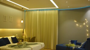 A modern hotel room with a bed, a sofa, a small table, and a curtain. - Luxury Skyline Studio • Near Cyberhub & Metro • NirviiHomes (Gurugram)