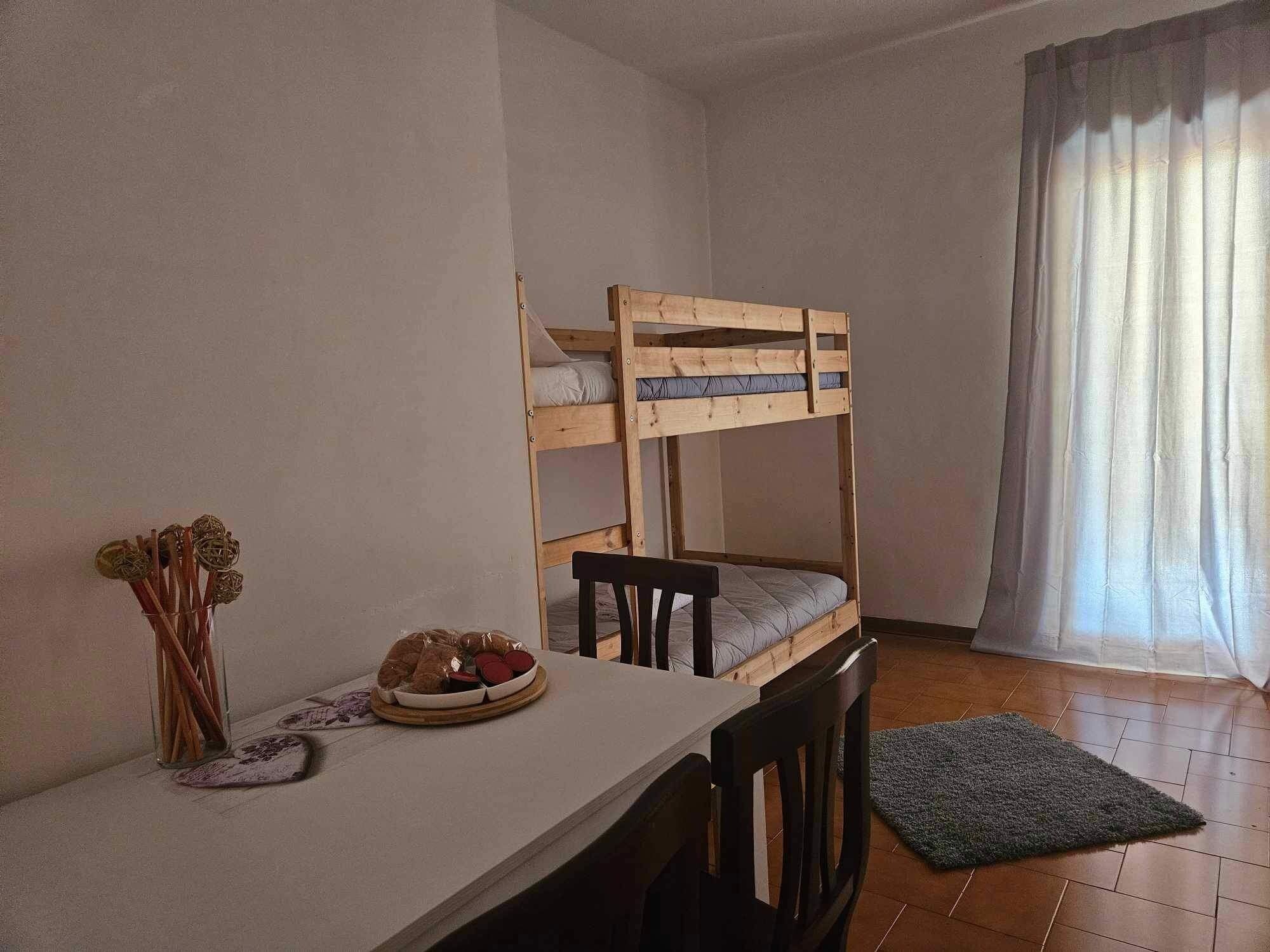Une chambre avec un lit superposé, une table, une chaise et un petit tapis.