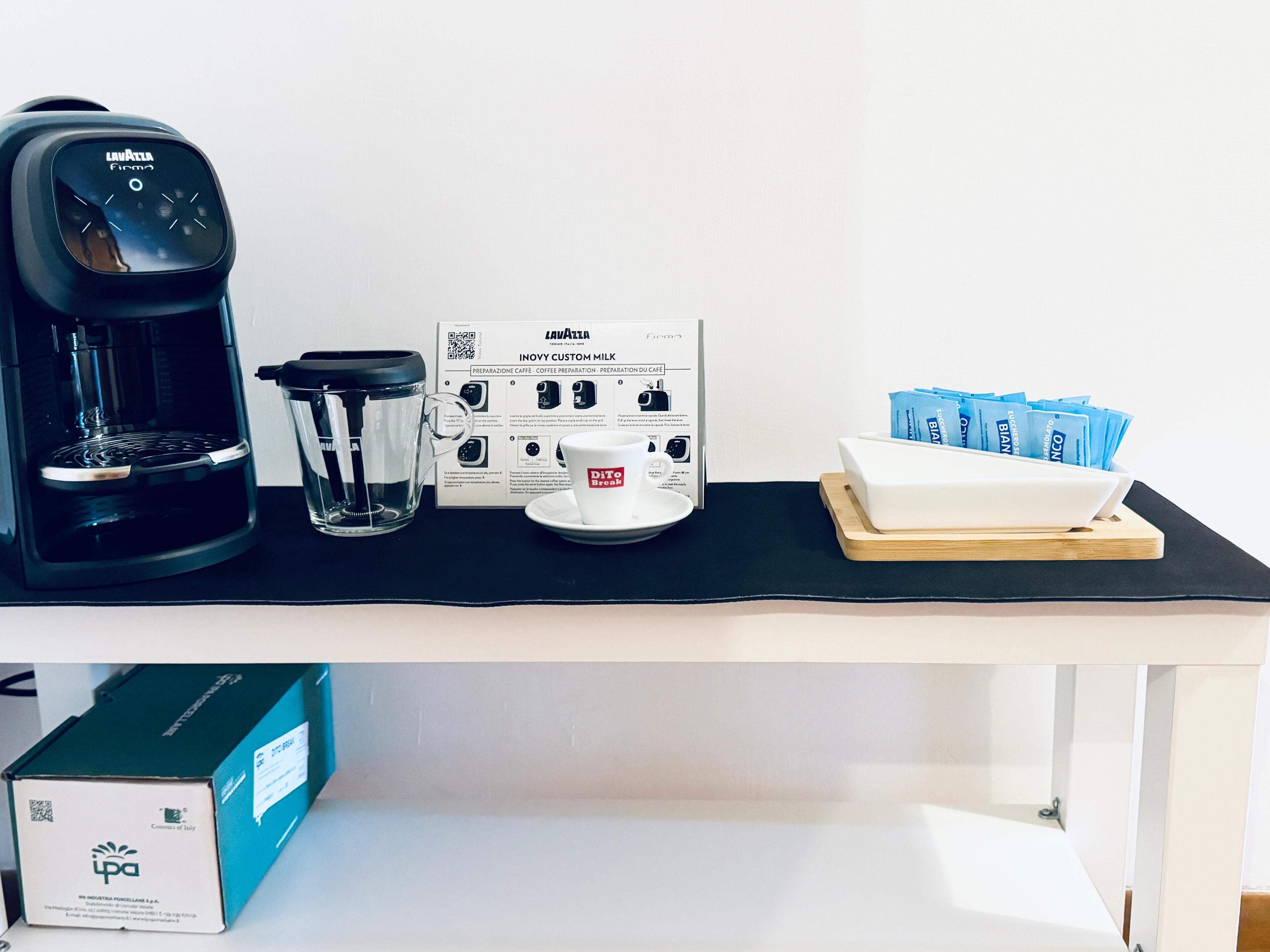 Une machine à café, une verseuse en verre, une boîte de dosettes de café et une tasse à café sur une table.