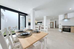 A modern dining area with a wooden table set for four, white chairs, and a glass of water. - White House Apartment • Marina 5 min (Puerto Calero)