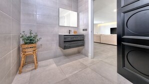 Un baño moderno con baldosas grises, un taburete de mimbre, un espejo y un mueble de madera oscura.