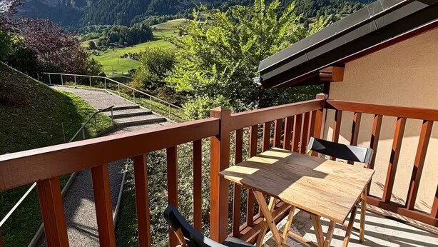 Un balcon avec une table et des chaises en bois, offrant une vue sur un paysage montagneux.