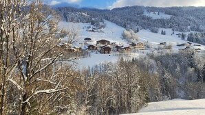 Un village enneigé, avec ses maisons traditionnelles en bois, une piste de ski et un paysage boisé en arrière-plan.