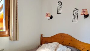 Une chambre à coucher avec un lit en bois, une literie grise, une fenêtre avec des rideaux et des lampes fixées au mur.