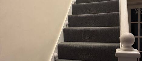 A staircase with a textured carpet, white balusters, and a white handrail.