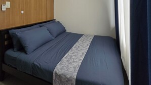 A single bed with a blue bedspread and pillows, a wooden headboard, a ceiling light, and a window with curtains. - WELCOME TO YOUR HOME AWAY FROM HOME. OUR UNIT HAS COMPLIMENTARY SECURE PARKING (Pasay City)