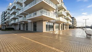 Een modern appartementencomplex met meerdere balkons, een geplaveid pad en een bankje.
