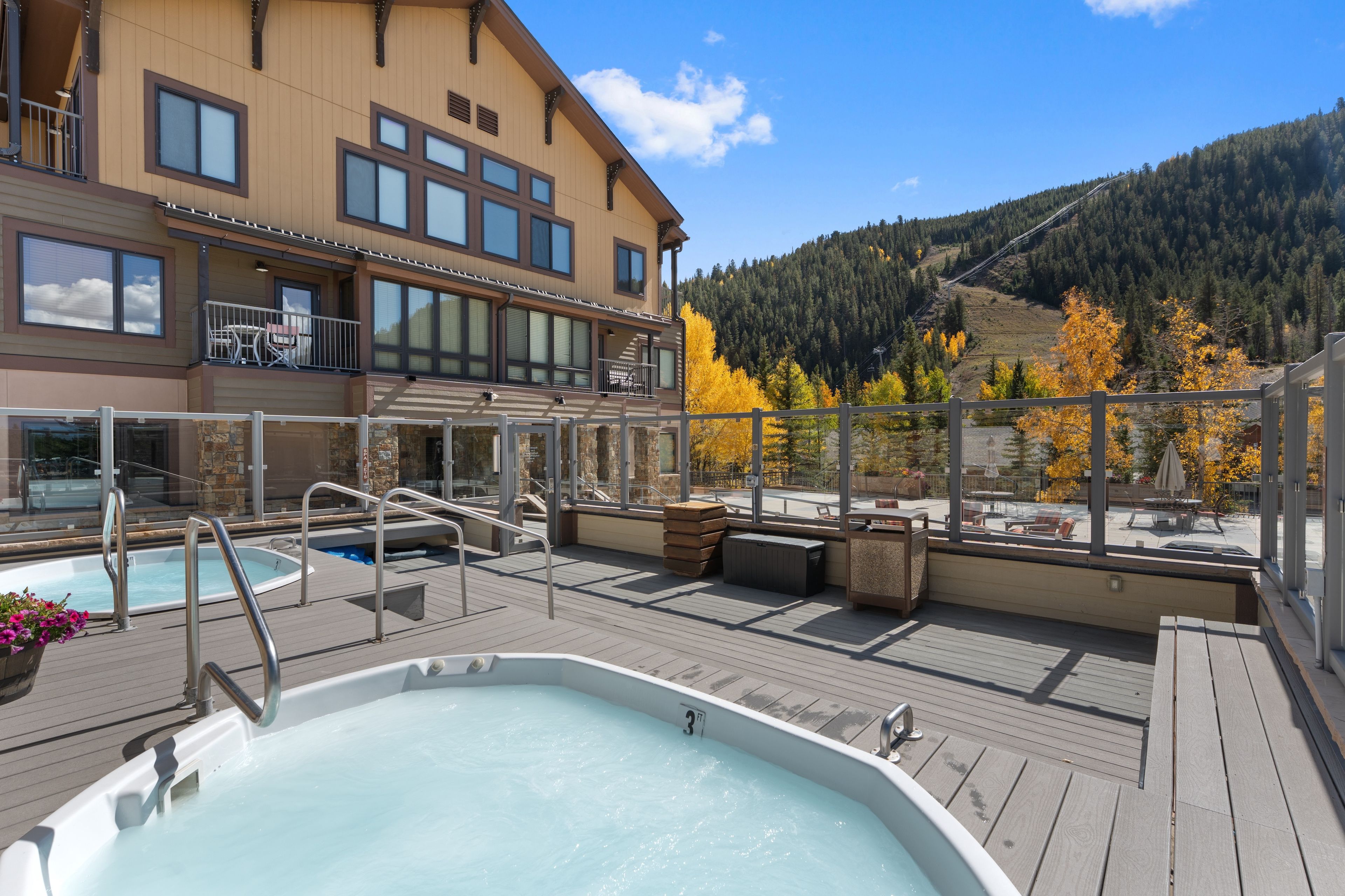 A rooftop pool area with a hot tub, outdoor seating, and a view of a forested mountain.
