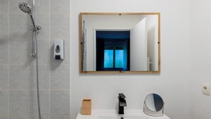 Une salle de bain moderne équipée d’une douche, d’un lavabo, d’un miroir et d’une fenêtre donnant sur un espace verdoyant.