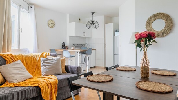Un salon moderne avec un canapé, une table basse et un coin repas comprenant des chaises et un vase de fleurs.