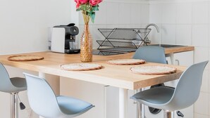 Une cuisine moderne avec des meubles blancs, une machine à café, un vase rempli de fleurs et un luminaire suspendu noir au design original.