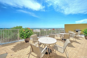 Eine Terrasse mit rundem Tisch und Stühlen, einem Grill und Blick aufs Meer.