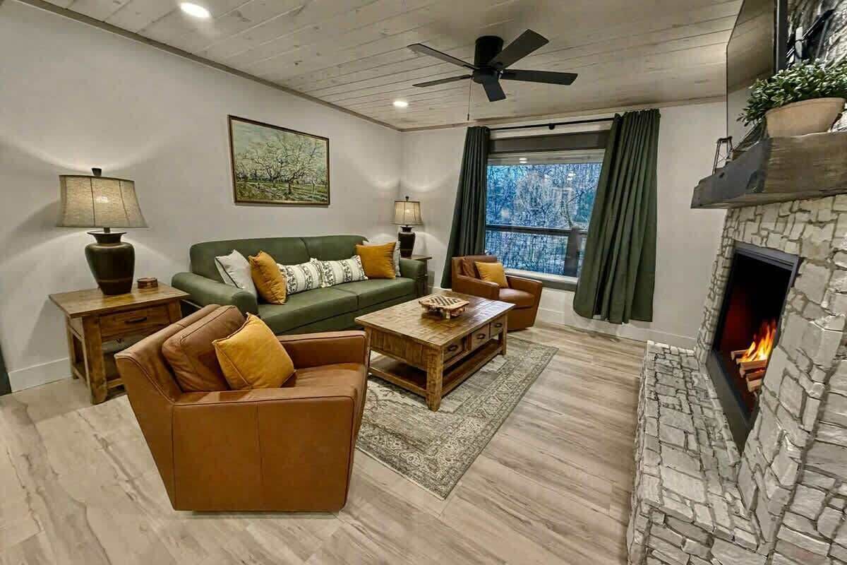 A living room with a stone fireplace, a green sofa, a brown leather sofa, a wooden coffee table, and two lamps.