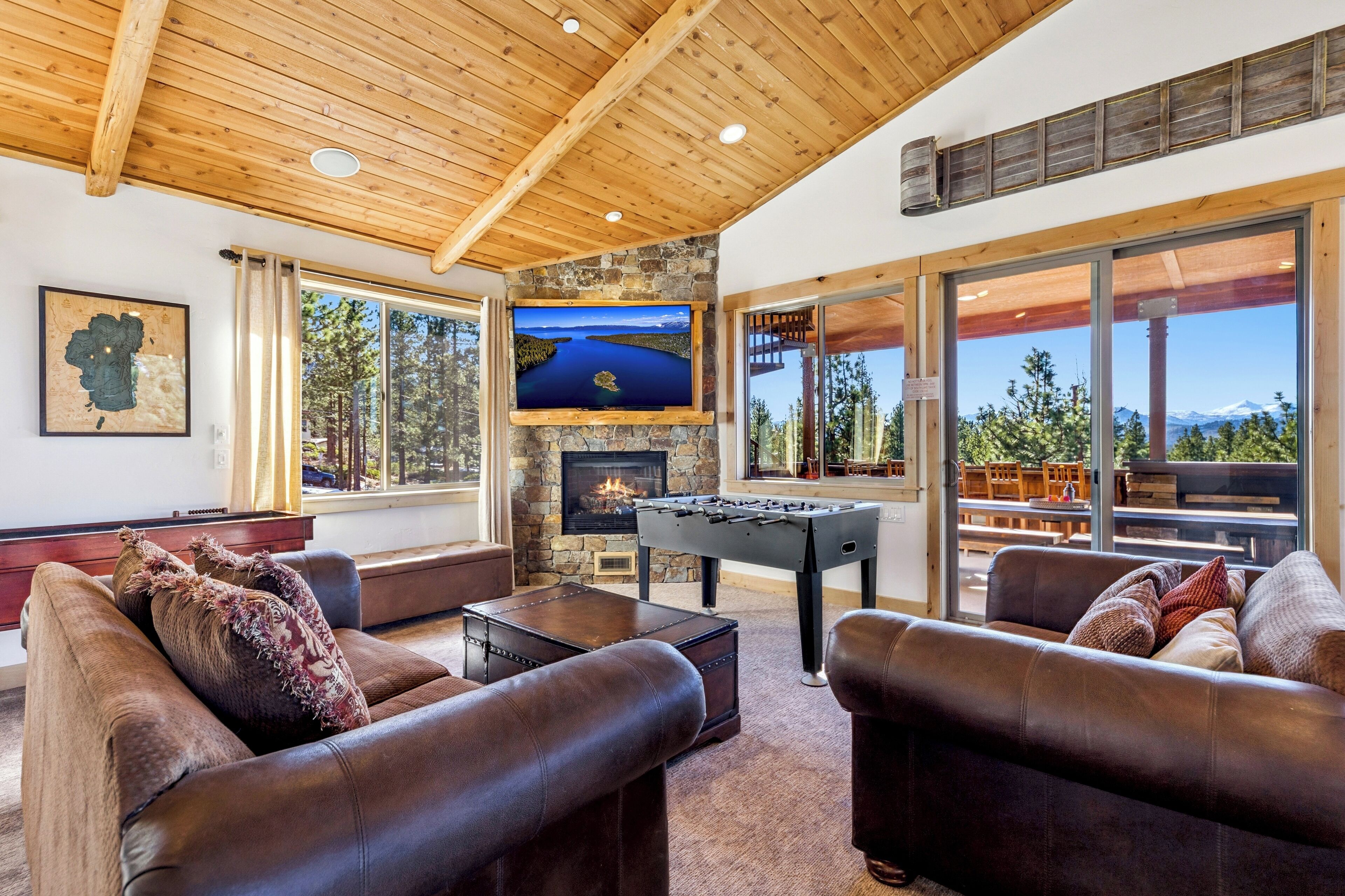 Una sala de estar acogedora con sofás de cuero, una mesa de fútbol, una chimenea de piedra y una pantalla de televisión grande.