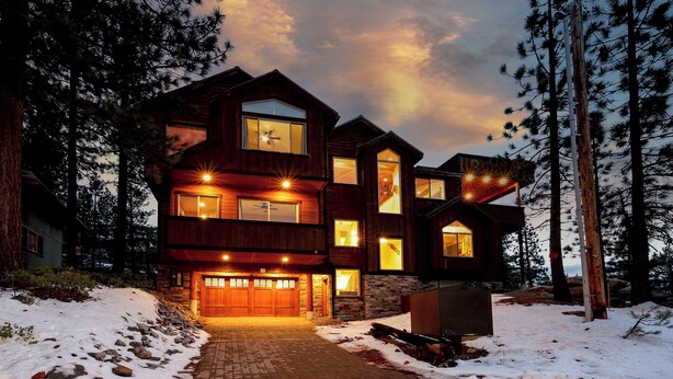 A multi-story wooden house with large windows and a garage, surrounded by trees and snow. - Heavenly Luxe Chalet - Hot Tub, Theatre, Game Room (South Lake Tahoe)