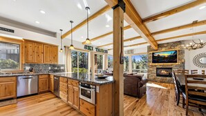 A spacious kitchen with wooden cabinets, granite countertops, and a stone fireplace. - Heavenly Luxe Chalet - Hot Tub, Theatre, Game Room (South Lake Tahoe)