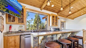 A kitchen with a stone island, wooden cabinets, and a large window offering a view of trees. - Heavenly Luxe Chalet - Hot Tub, Theatre, Game Room (South Lake Tahoe)
