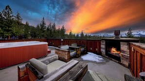 An outdoor seating area with a hot tub, fire pit, and wooden furniture against a backdrop of a mountainous landscape and a colorful sky. - Heavenly Luxe Chalet - Hot Tub, Theatre, Game Room (South Lake Tahoe)