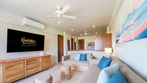 Een moderne woonkamer met een flatscreen televisie, banken, poefs, plafondventilatoren en een houten kast.