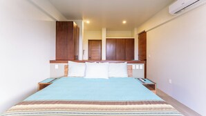 Een slaapkamer met een bed, een houten hoofdbord, nachtkastjes en een airconditioner.