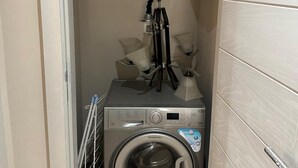 Ett litet och praktiskt tvättrum med en tvättmaskin med frontmatning, ett torkställ och en liten hylla med en vattenkokare och andra tillbehör.