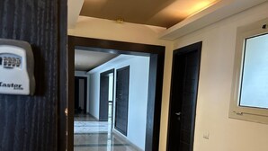 En hotellkorridor med modern design, med en lång hallgång som har mörkt och ljust kakel på golvet, svarta dörrar och ett tak med infälld belysning.