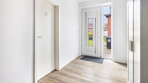 A hallway with a white door marked with the number 9, a glass door leading outside, and a wooden floor.