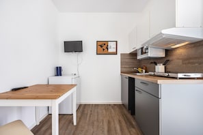 A compact kitchen with a wooden table, white cabinets, a microwave, and a wall-mounted TV.