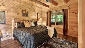 Ein Schlafzimmer einer Holzhütte mit einem Bett, einem Deckenventilator, einem Fenster mit Vorhängen und einem Nachttisch.