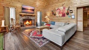 Ein Blockhaus-Interieur mit Kamin aus Stein, einer weißen Ledersofa, Holzboden und einem Gemälde vom Sonnenuntergang.